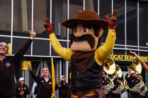 person in oversized Pistol Pete costume in front of a marching band