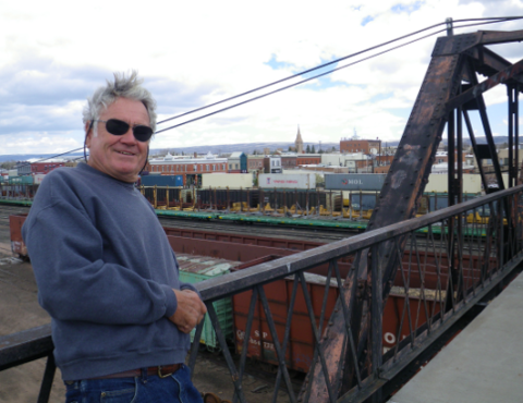 Man poses leaning on the railing of a bridge