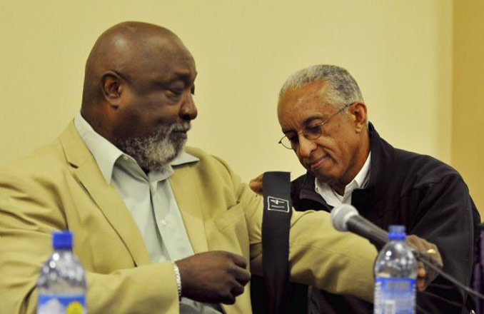 Mel Hamilton, left, extends his arm for former teammate John Griffin to tie on a black armband at the 40th anniversary of the Black 14 event, 2009. Andy Carpanean photo, Laramie Boomerang.