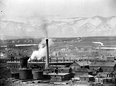 View of Burlington railyard in Sheridan, showing plume of steam from roundhouse and stacks of raw and treated railroad ties adjacent to the tie-treatment plant.  Courtesy of Wyoming Room, Sheridan County Fulmer Public Library.