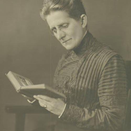 Woman in a high-collared drass reads a book she holds in her hands