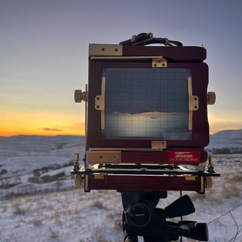 closeup of the large format camera, focused on the landscape before it, as the sun rises in the distance