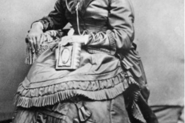 Black woman in an elaborately ruffled dress poses while seated.