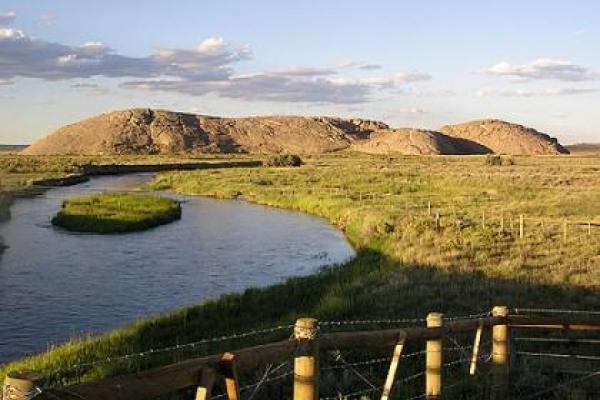 early morning light on rounded hills nar a wide river on a treeless plain with fenceposts in the foreground