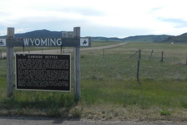 historical marker headlined "Rawhide Buttes" on a roadside with a road leading off into the distance through a treeless plain toward low hills in the distance