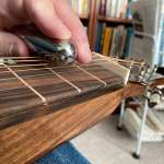 On the neck of a steel guitar, the strings are raised by a nut well above the frets and the player, with his left hand, moves a steel or tone bar along the strings to define the notes. Strings are then plucked by the right hand to create the sounds. Movements of the bar create the wavering tones associated with the instrument. Author photo.