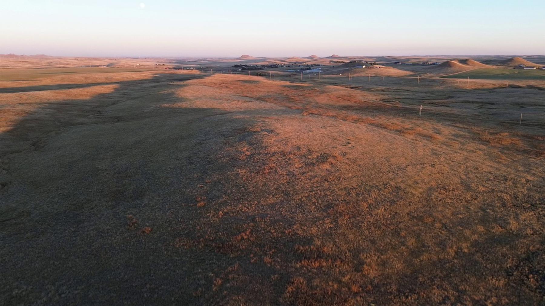 The site of the fight on Bonepile Creek today. The White men dug rifle pits near the top of the knoll in the foreground; Bonepile Creek flows down the shadowed draw to the left. This photo is looking southeast; Wyoming Highway 50, the road from Pine Tree Junction to Gillette, is in the distance. Author photo.