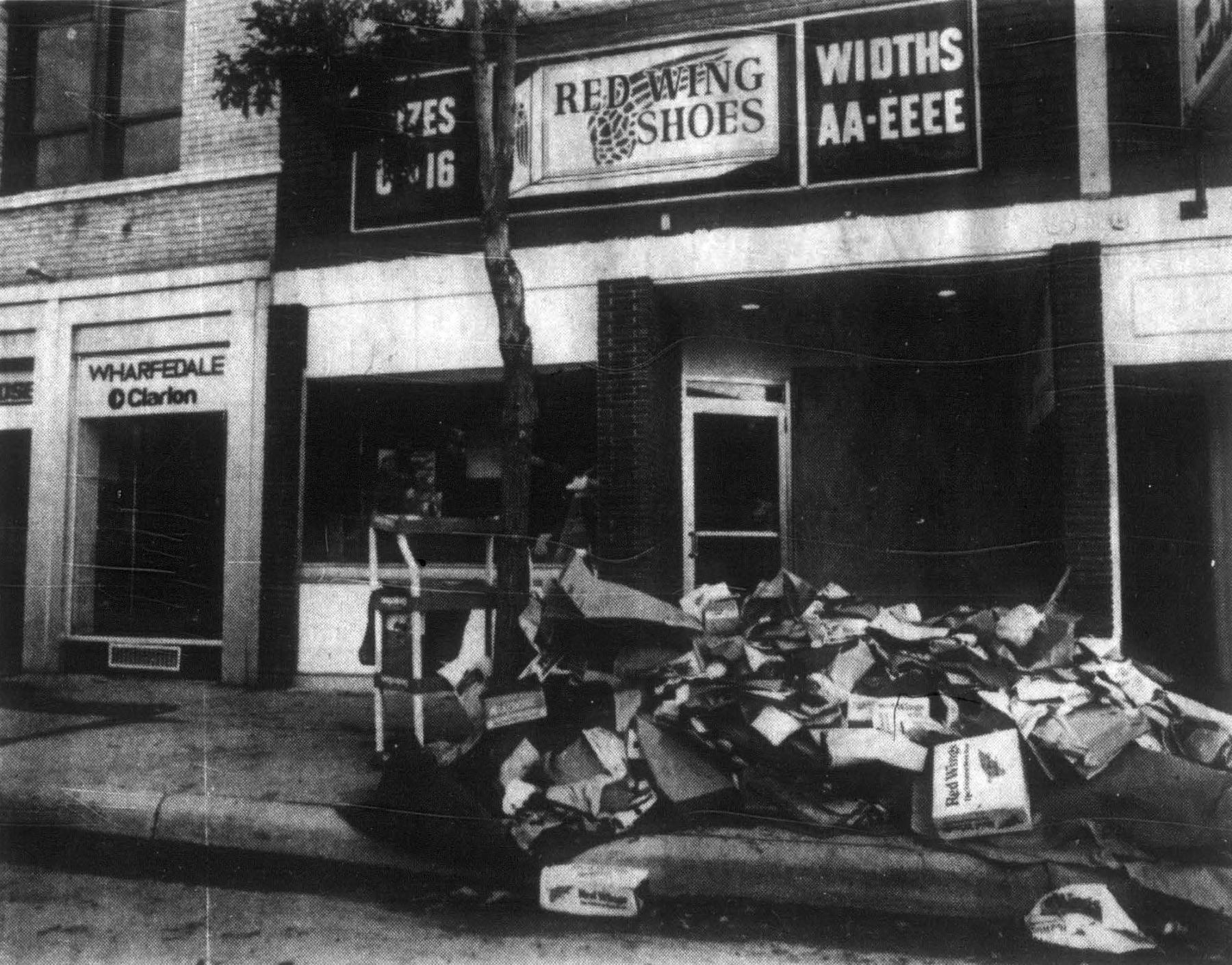 Downtown businesses continued cleanup efforts days after the flood, with piles of water-damaged merchandise and debris lining the streets. Red Wing Shoes on 17th Street, like many downtown establishments, suffered extensive damage from the floodwaters. Downtown Cheyenne street storefronts with a large pile of debris in front on the sidewalk