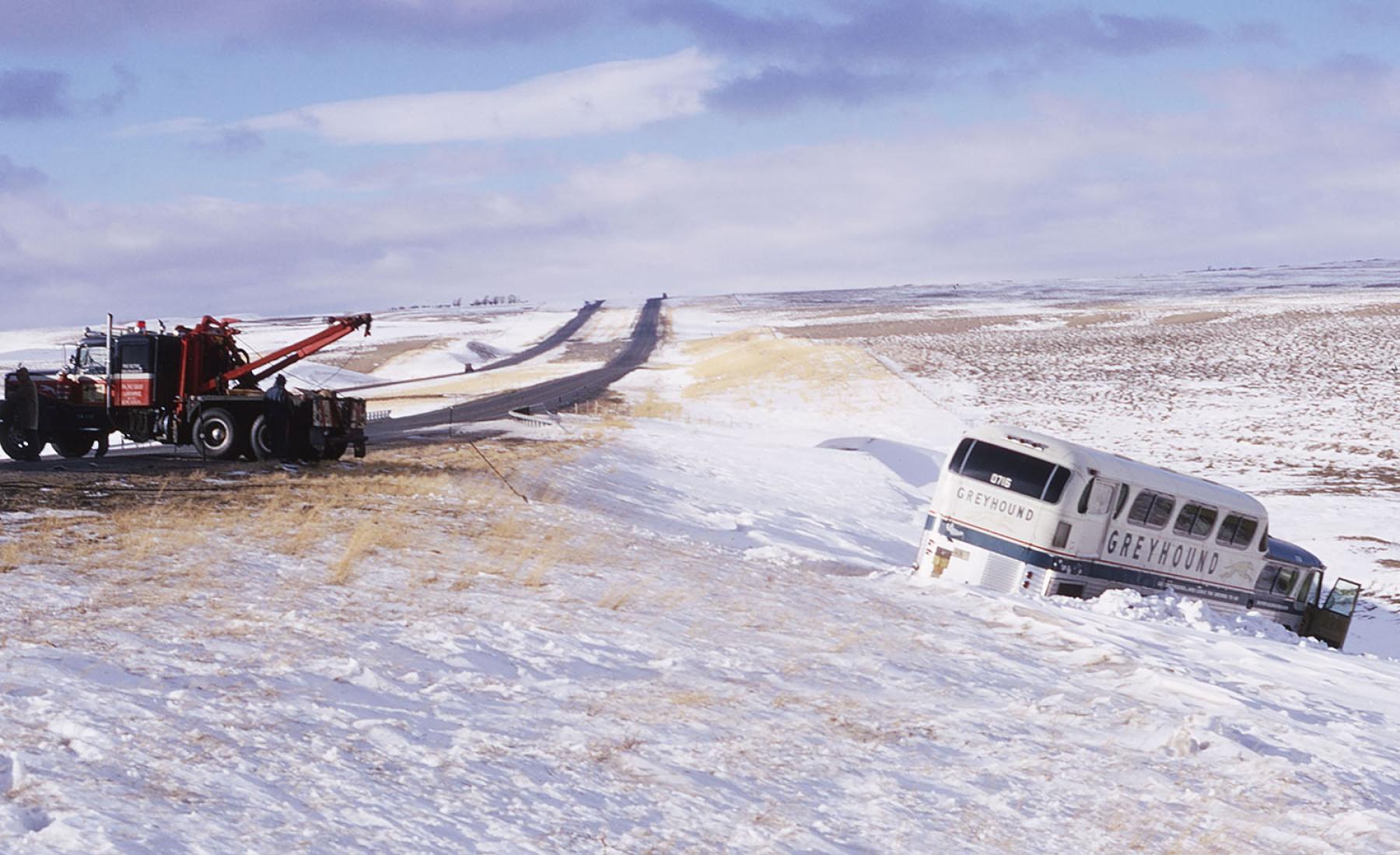 Interstate 80 near Arlington, December 1972. Truck on highway trying winch up a Greyhound bus that has run off the road into adrift on a snow-swept landscape