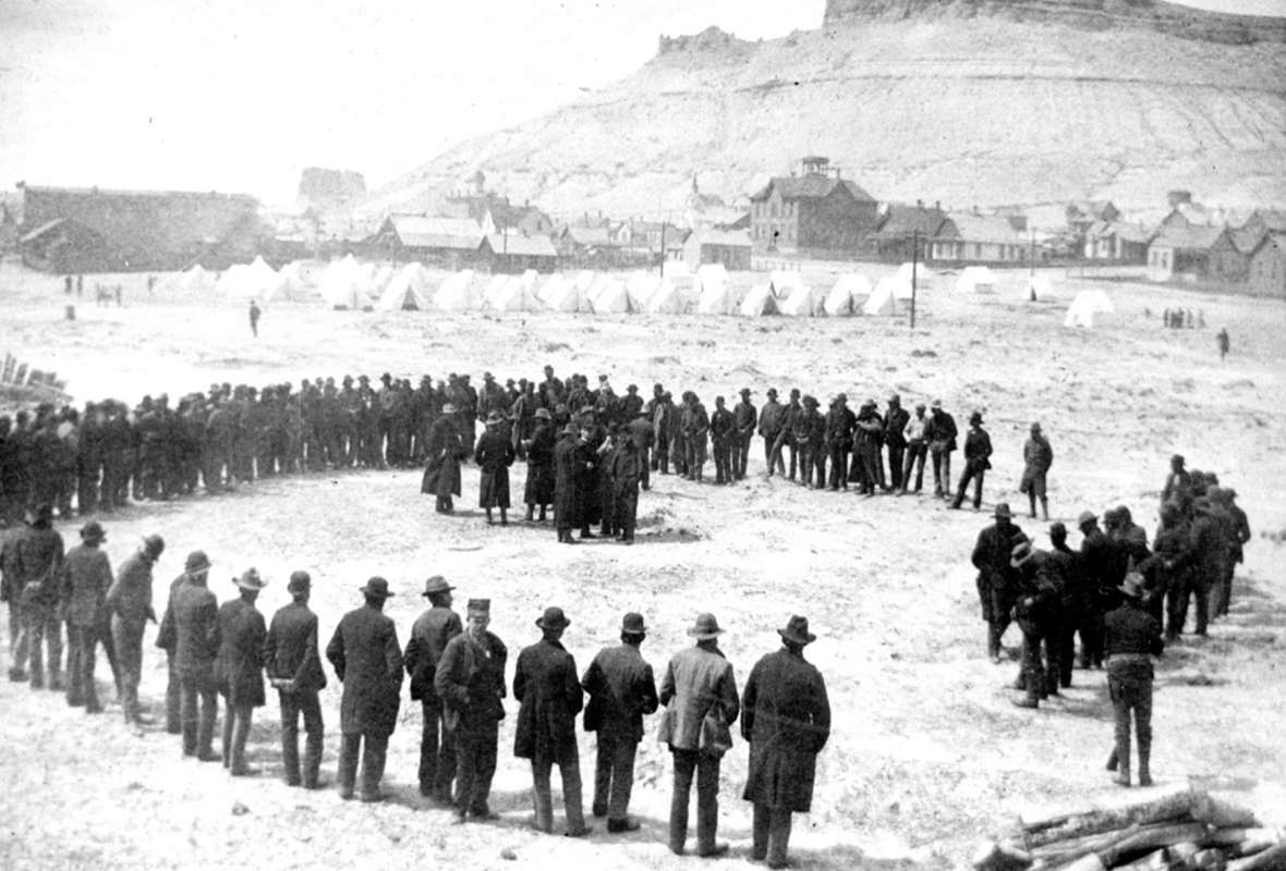 Coxeyites at morning roll call in camp on the edge of Green River, Wyo., May 16, 1894. Troops were called in from Fort Russell in Cheyenne to guard the protesters until the proper warrants could arrive and they could be sent back to Idaho. Sweeetwater County Historical Museum.