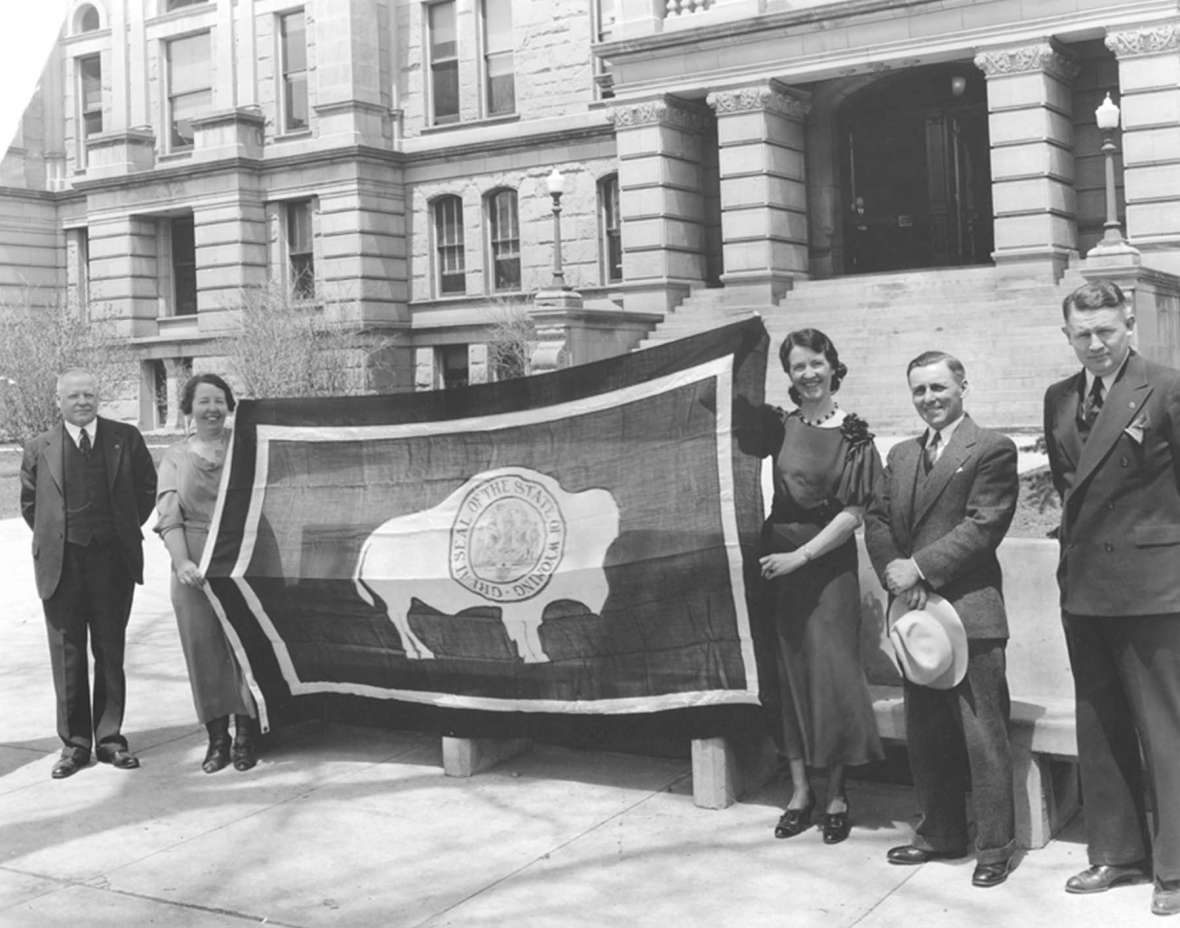 In this photo from 1935, state politicians and staffers hold up a Wyoming State flag before it was flown at the California Pacific International Exposition that year in San Diego. Left to right:  Leslie Miller, Wyoming governor; Margaret Burke, assistant state Historian; Ruth Kingham, secretary; Scotty Jack, state auditor; Lester Hunt, secretary of state. The extra strip of white binding on the viewer’s left  appears to show the bison faced away from the flagpole—contrary to what Grace Hebard would have wished. Wyoming State Archives.