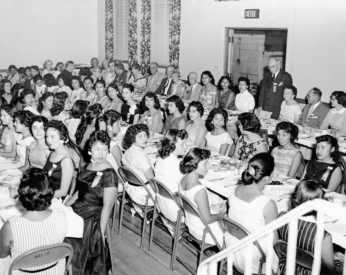 These women wear 1950s party dresses and modern hairstyles at a dinner for Miss Indian America contestants and judges at Sheridan’s Kalif Shrine Mosque. Howard Sinclair is standing. The reigning Miss Indian America would be expected to wear tribal regalia throughout the coming year while serving in her official capacity as a goodwill ambassador. Lochrie Collection, Montana Historical Society. 