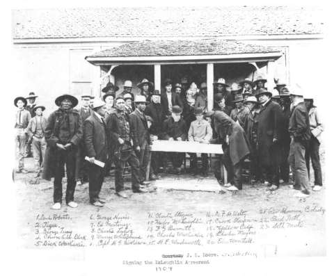 Northern Arapaho Chief Yellow Calf signs the agreement ceding lands north of the Wind River, 1904. Congress, without consulting the tribes, later amended it. Government negotiator James McLaughlin is at the table in a dark coat. Dick Washakie, son of the recently deceased chief of the Eastern Shoshones, is standing in the front row on the left, hat in hand, badge on his vest. American Heritage Center, University of Wyoming.