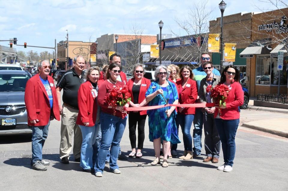 Ribbon cutting in downtown Gillette 2023. Photo by Mary Kelley. A group of adults poses around a ribbon with the center person holding scissors. They are on a street in a downtown area.