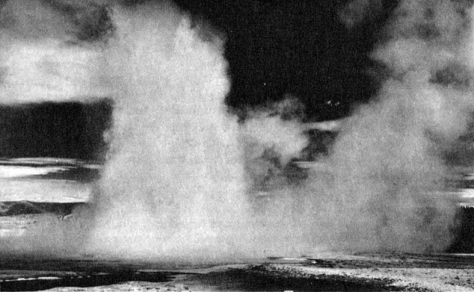 clouds of steam and jets of water erupt from a geyser basin