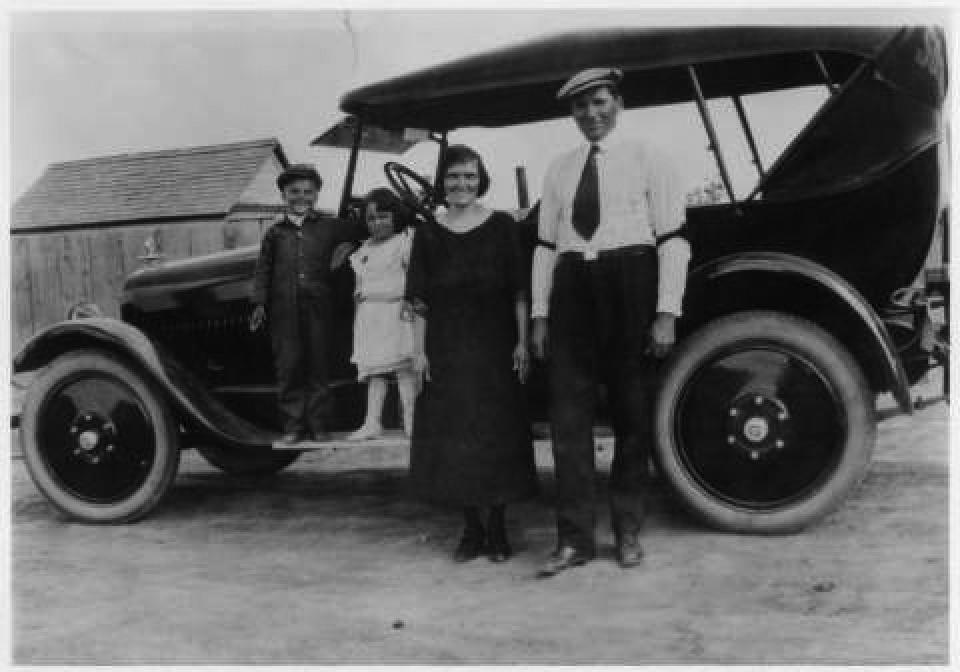 The Taucher family in Superior, Wyo., early 1920s. L. to R.: John Taucher; Kathy Karpan's mother, Pauline Taucher; Karpan's grandparents Josephine and Frank Taucher. Photo courtesy Wyoming State Archives. A man and woman pose smiling on front of a 1920s automobile, with a boy and girl standing on the running board.