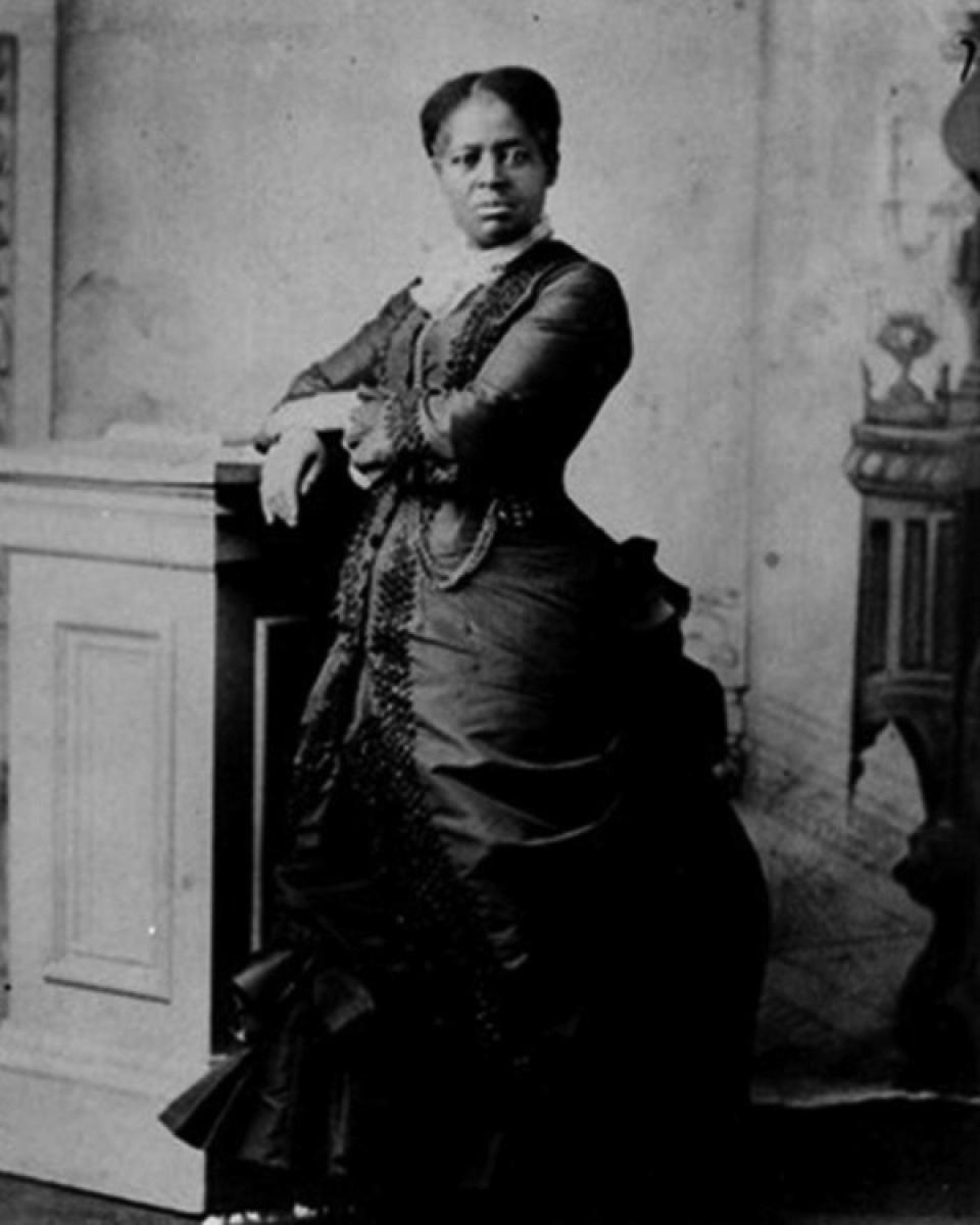 Marchbanks in a dress given to her in 1881 for her culinary talents. Photo courtesy of the Museum of the American West, Lander, WY. Portrait of a Black woman wearing a high-necked dress with a bustle, standing next to a podium