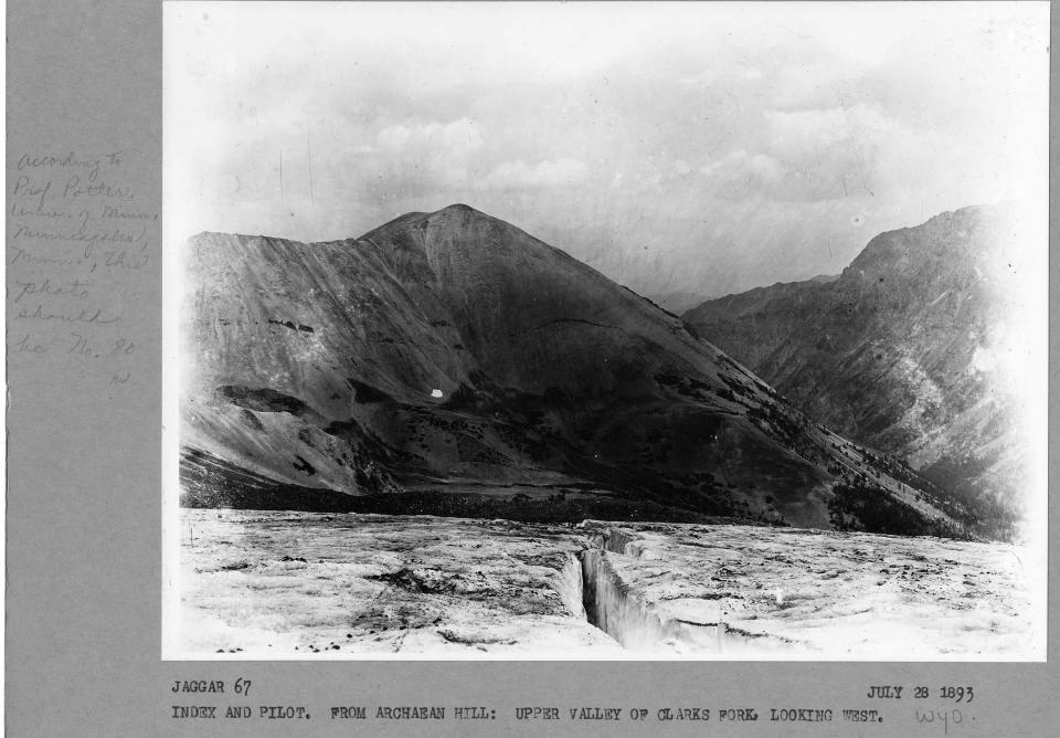 black and white photo looking down thick glacial layers and crevasse toward mountains in the distance.
