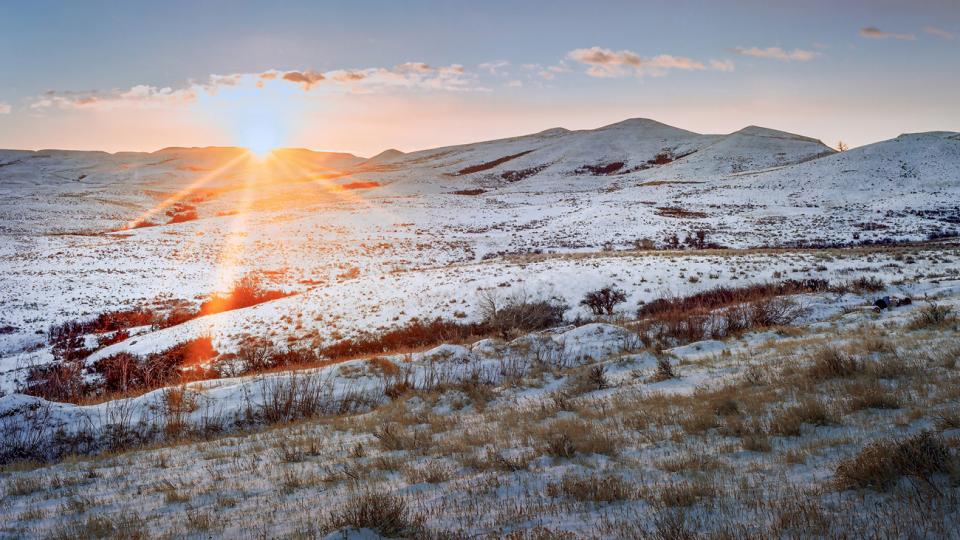 sun rising over a rolling, snow-swept plain