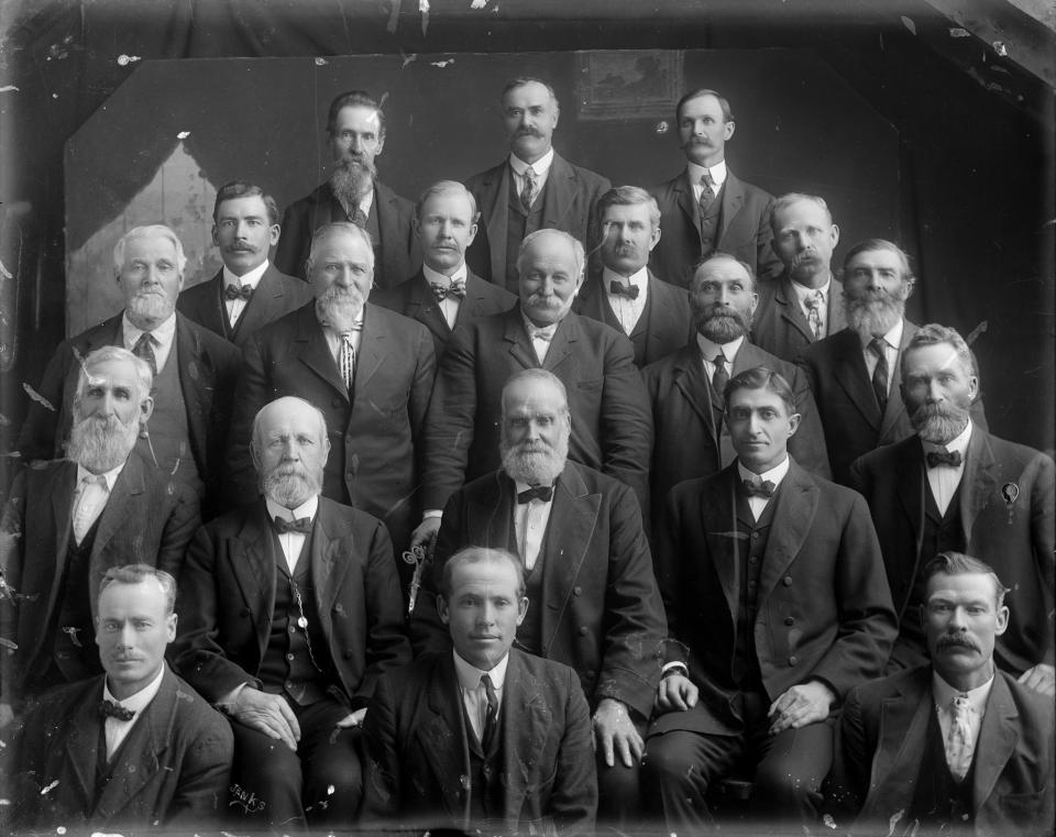 A group of twenty men in suits pose together for a formal portrait
