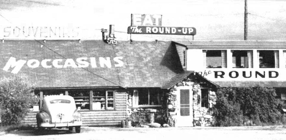 low lying building with the word "Moccasins" spelled out on a shingle roof, and the word "Round" under the second floor windows