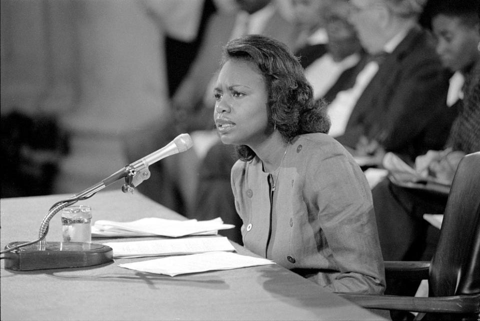 Anita Hill speaks into a microphone while seated at a table during a Senate hearing