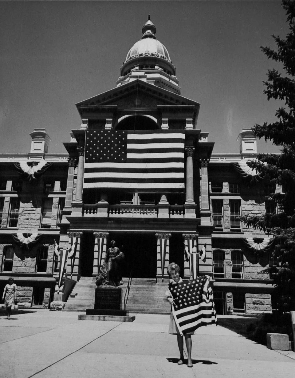 A woman holds an American flag while standing in front of a large building draped with an enormous American flag.