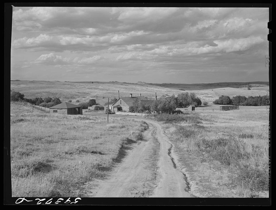 Open plains with a dirt road leading to a ranch house in the distance