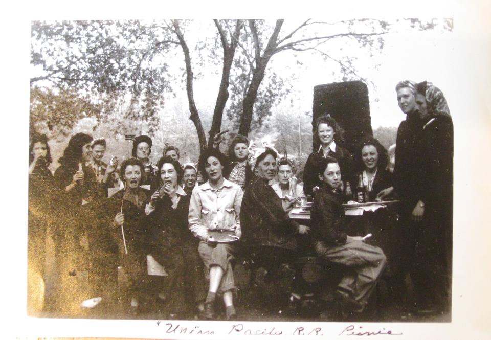 Group portrait of many seated women smiling, at a picnic table in a park