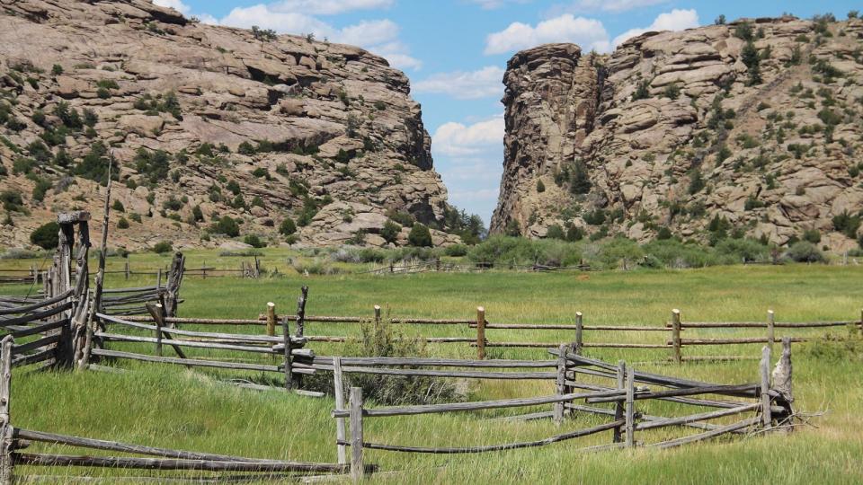 rail fences cordoning off a grassy area in front of hight rock cliffs either side of and open slot