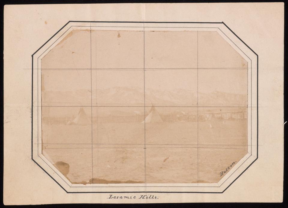 very faded sepia image of open area with a couple of teepees in front of a long one-story log building with mountains in the distance. There is a grid drawn over the image and the words "Laramie Hills" at the bottom