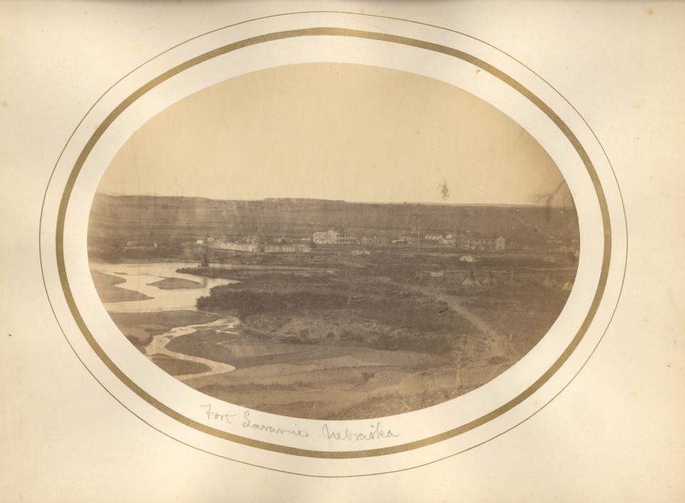 sepia toned landscape in oval mat, dimly showing a wide treeless landscape with a winding river and numerous buildings in the distance