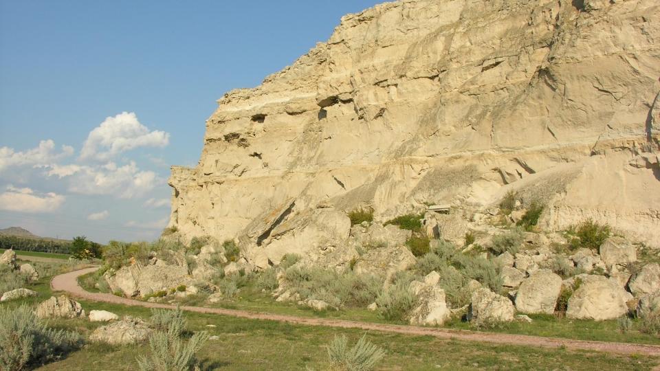 wall of a sandstone bluff with a narrow dirt road at its base