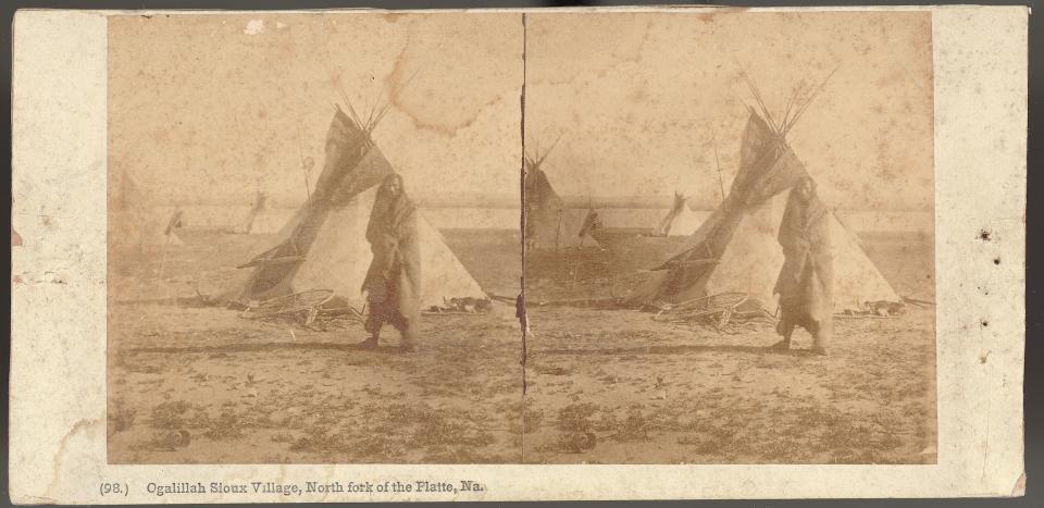 stereograph (two of the same image side-by-side) for a person wrapped in a robe standing in front of a teepee on a plain with three more in the distance