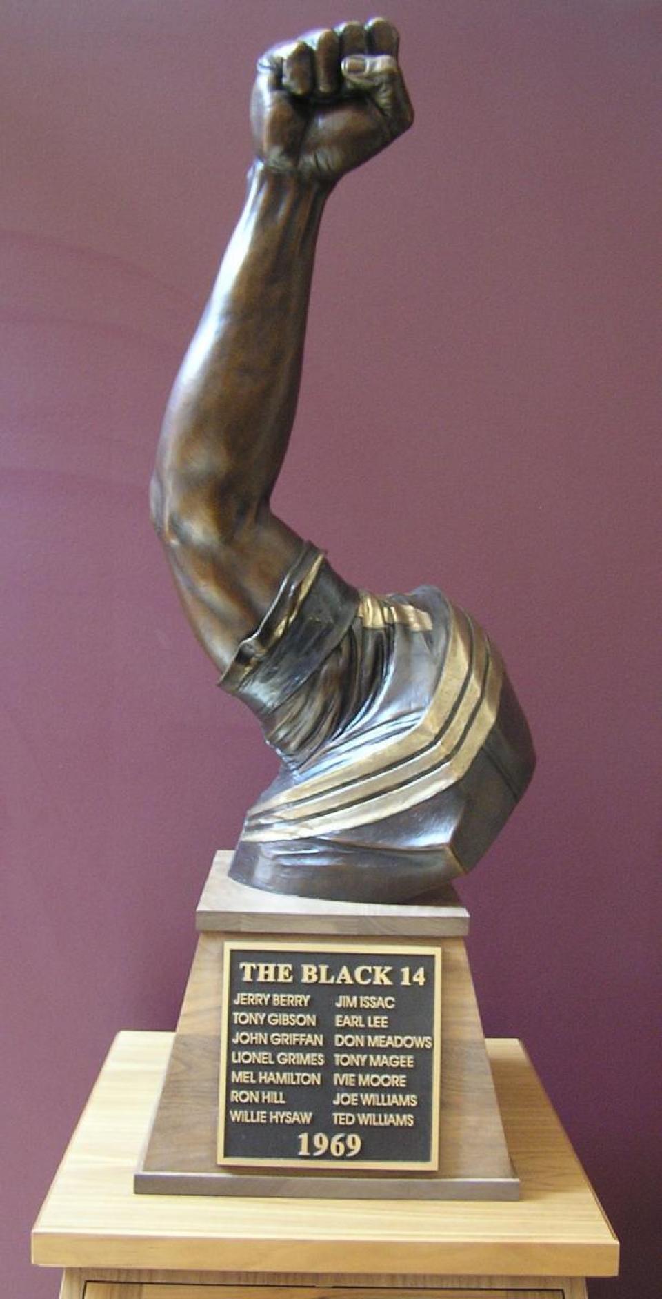 Bronze sculpture of a fist on a raised arm, mounted on a pedestal with the words, "The Black 14" and the names of each of the men who were among the 14