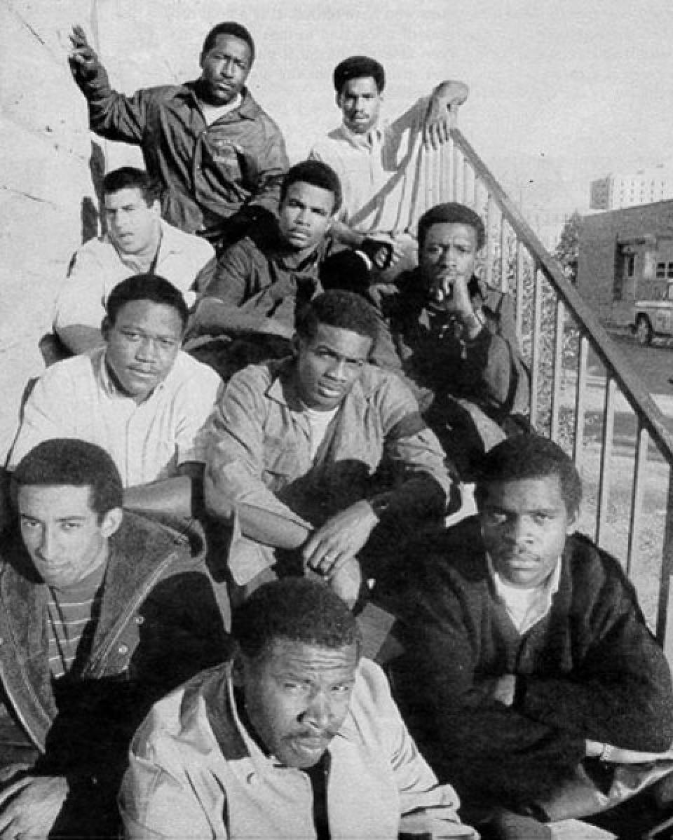 ten casually dressed Black men seated on a staircase outside, in ascending rows of three, two, three, and two
