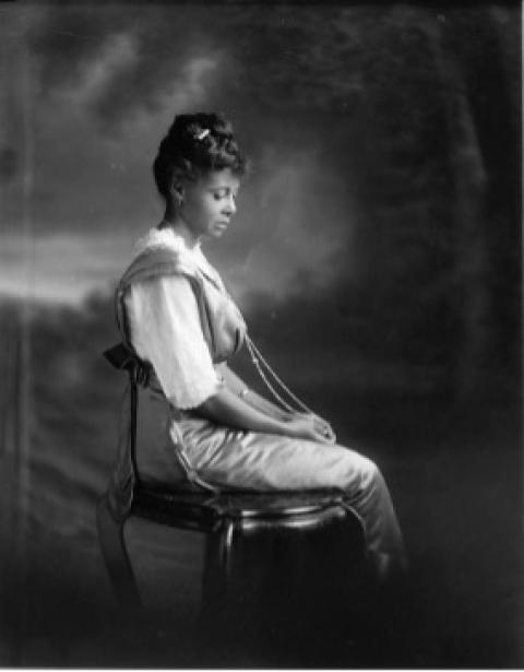 Born in 1875 to Jeff and Helen Thompson, DeMarge was reportedly the first Black child born on record in the Wyoming Territory—only five years after the 1870 election. A young Balck woman poses ina chari with downcast eyes