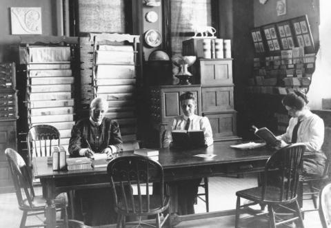 Wergeland and Hebard around 1910 with UW student and Hebard protégé Agnes Wright Three women in long dresses reading and writing, seated at a table in a room with cupboards and racks of papers