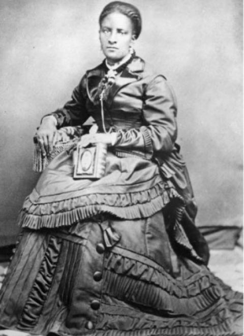 Nancy Phillips’s talent as a seamstress is clearly on display in her portrait. Black woman in an elaborately ruffled dress poses while seated.