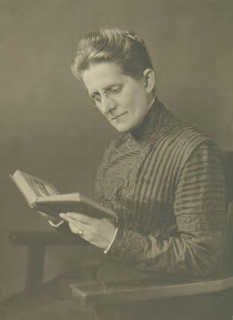 Woman in a high-collared drass reads a book she holds in her hands