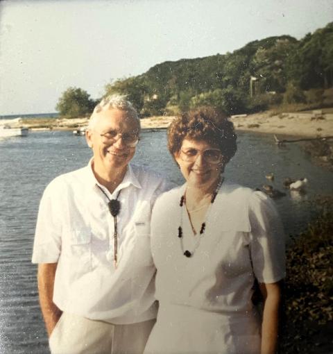 A couple poses smiling in front of a lake