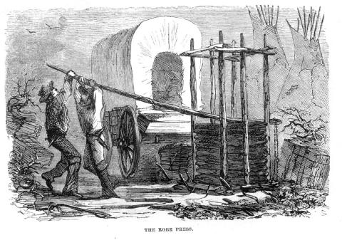 Etching of two men pulling down a long log lever above a pile of buffalo hides stacked in a frame, in front of a covered wagon 