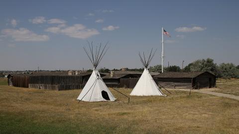 open area with two teepees in front of a one-story log fortress