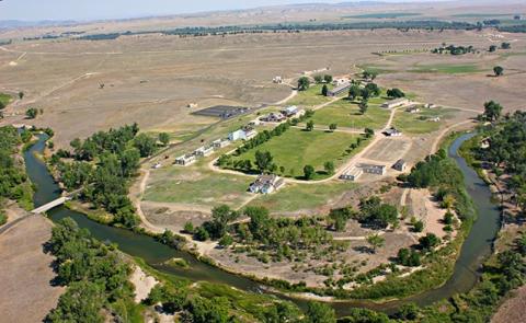 aerial view of plains and vegetated river bend flanking an area of irrigated lawns and several buildings that don't appear to have roofs