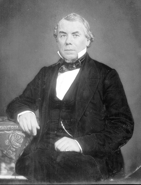 formal portrait of a seated gray-haired man in a dark suit and high collar with tie