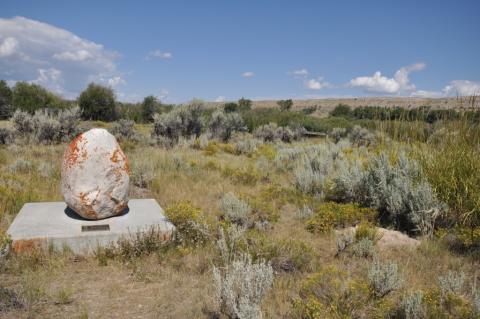 egg-shaped rock on a concrete slab with a label on an open dry plain with sagebrush and low vegetation