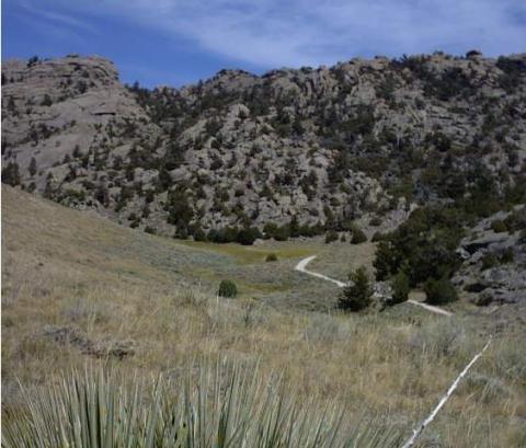 View up dirt road through a shallow valley toward some rocky ridges