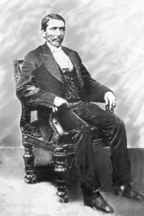 man in a three-piece-suit sitting in a heavy wood armchair