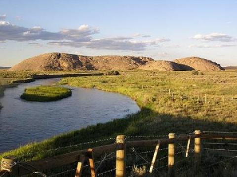 early morning light on rounded hills nar a wide river on a treeless plain with fenceposts in the foreground