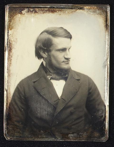 Photo of a dark-haired man with a sparse beard under his jaw, wearing a heavy suit coat